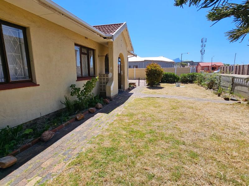 Front exterior view of a residential property featuring a paved walkway, dry lawn, and boundary walling.