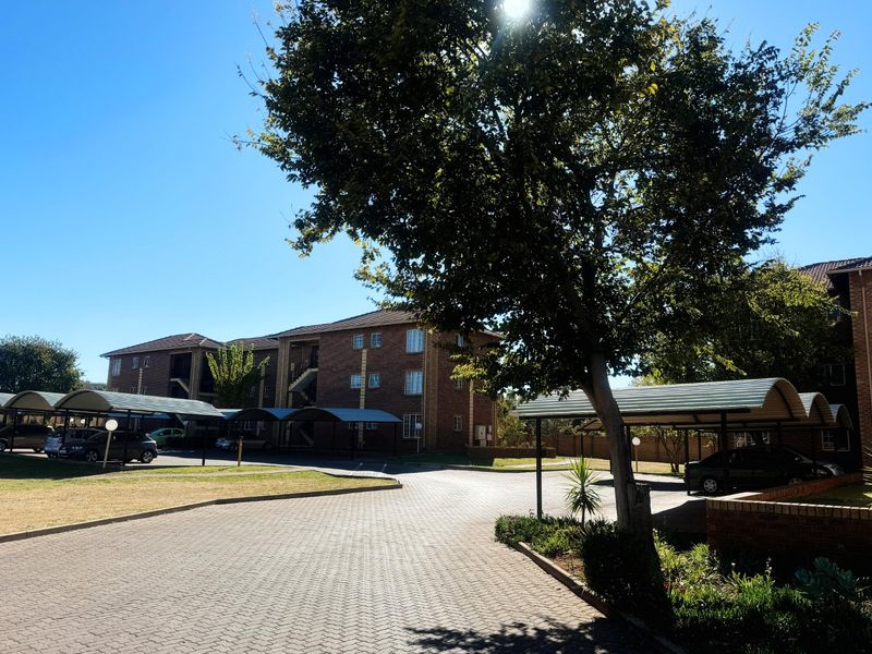 Exterior view of a brick apartment complex featuring paved driveways and covered carport parking bays.