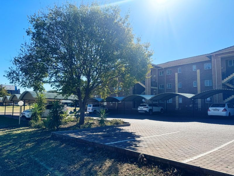 Exterior view of an apartment complex featuring a brick facade, paved parking area, and covered carport structures.