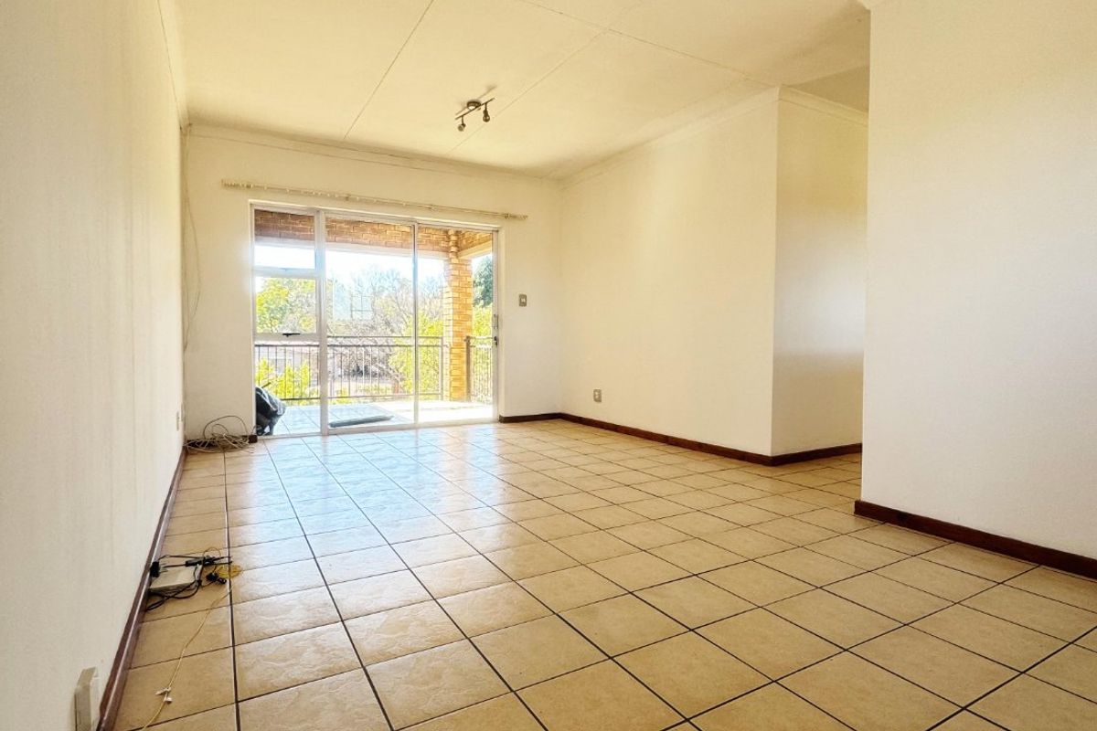 An empty, open-plan living area featuring neutral tiled flooring, coved ceilings, and a sliding glass door providing access to an outdoor balcony.