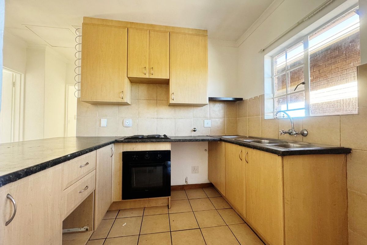 A functional kitchen featuring laminate cabinetry, built-in oven and hob, tiled backsplash, and double bowl sink, ready for a modern update.