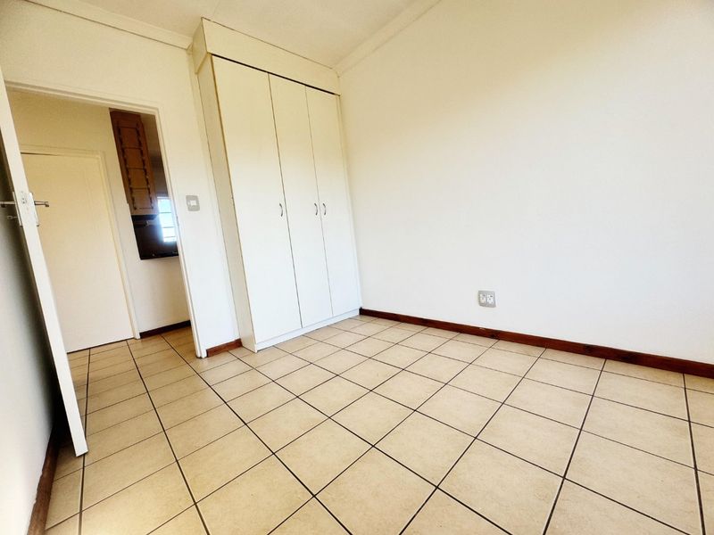 An empty bedroom featuring neutral ceramic floor tiles, white walls, and a built-in wardrobe with white cabinetry.