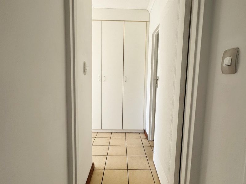 A clean, functional hallway featuring neutral tiled flooring and built-in storage cupboards, providing a bright and practical transition space within the apartment.