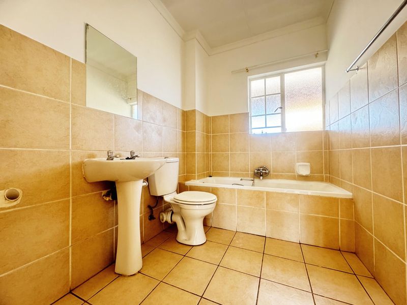 A functional bathroom featuring a pedestal basin, toilet, and built-in bathtub with neutral wall and floor tiling.