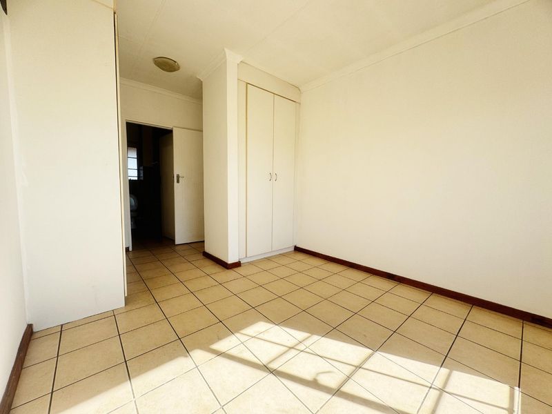 A bright, empty bedroom featuring neutral tiled flooring and built-in storage cupboards, offering a clean and versatile space ready for personalization.