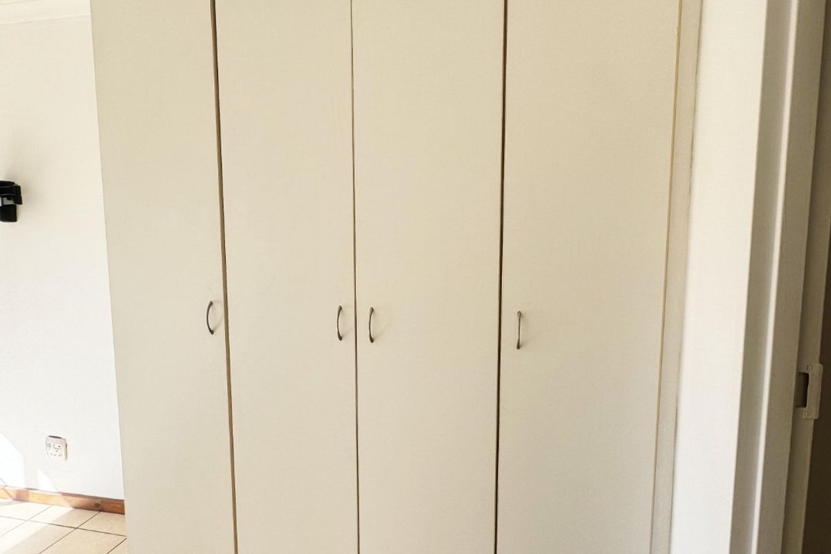 A bedroom featuring neutral tiled flooring and a large, white built-in wardrobe providing ample storage space.