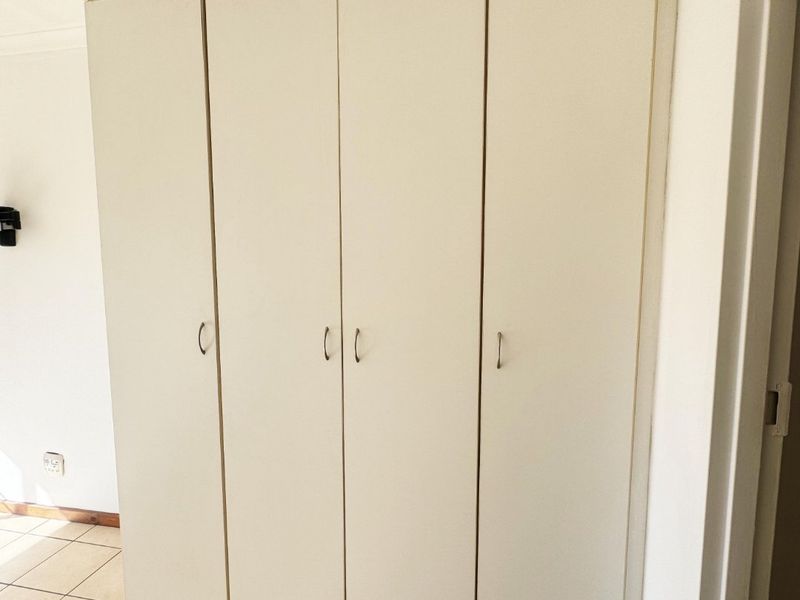 A bedroom featuring neutral tiled flooring and a large, white built-in wardrobe providing ample storage space.