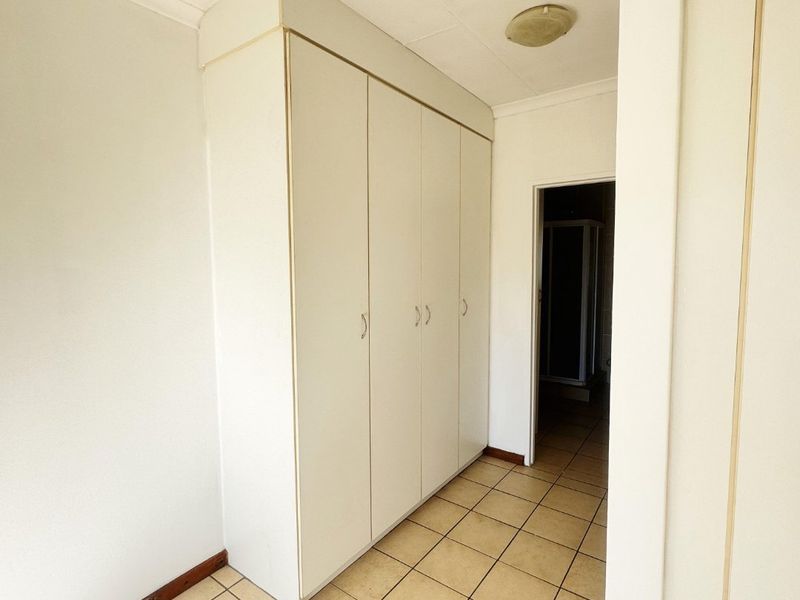 A functional hallway featuring built-in storage cupboards, ceramic tiled flooring, and neutral finishes, providing access to adjacent rooms.