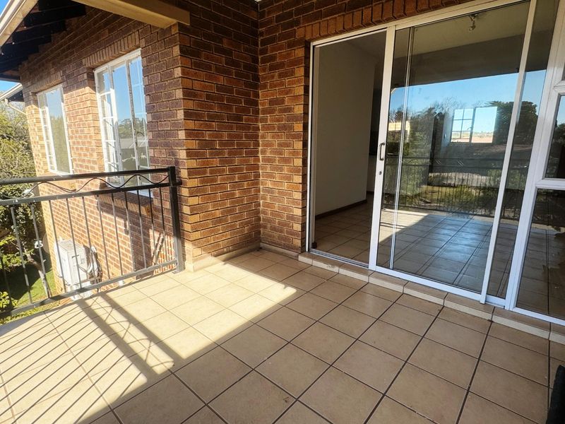 A spacious balcony featuring tiled flooring, exposed brick walls, and a wrought iron balustrade, accessible via large sliding glass doors.