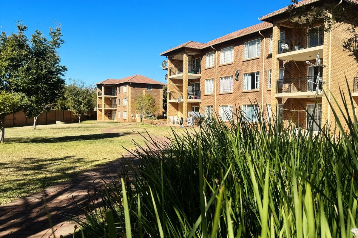 Exterior view of a multi-story apartment complex featuring face brick facades, private balconies, and well-maintained communal garden areas with paved walkways.