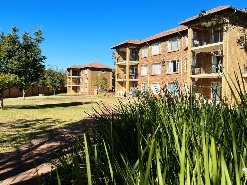 Exterior view of a multi-story apartment complex featuring face brick facades, private balconies, and well-maintained communal garden areas with paved walkways.