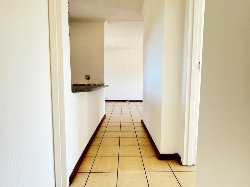 A bright, empty hallway featuring tiled flooring and a breakfast bar opening into the adjacent living space.