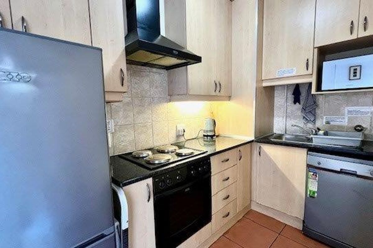 A functional kitchen featuring light wood cabinetry, black granite countertops, a built-in oven with extractor fan, and a stainless steel sink.