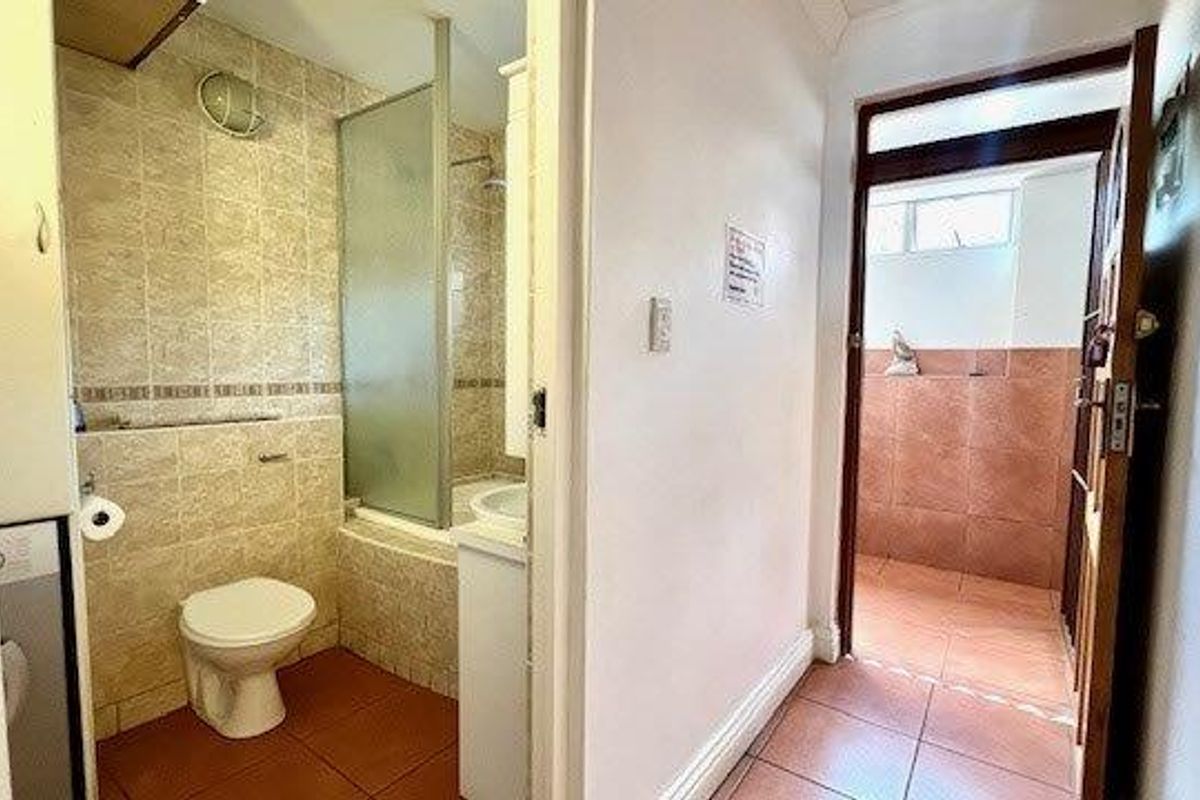 A functional bathroom featuring a shower-over-bath combination, tiled walls, and a standard toilet, adjacent to a tiled hallway area.