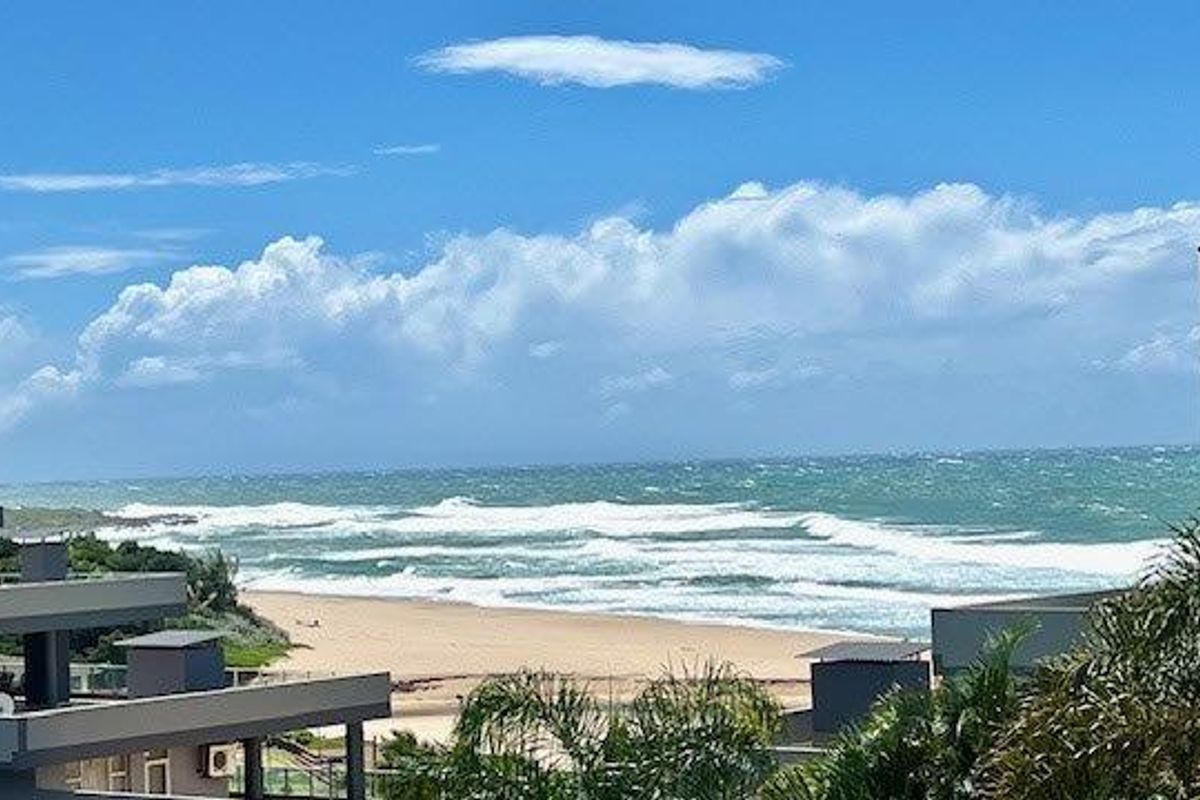 A scenic elevated view overlooking the coastline, featuring sandy beaches and ocean waves, captured from an apartment balcony.