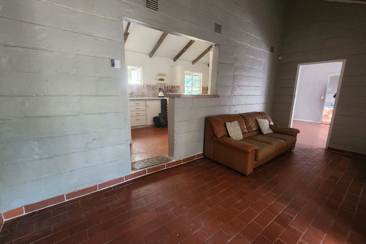 Living area featuring terracotta tile flooring, exposed beam ceilings, and a convenient pass-through window connecting to the kitchen space.