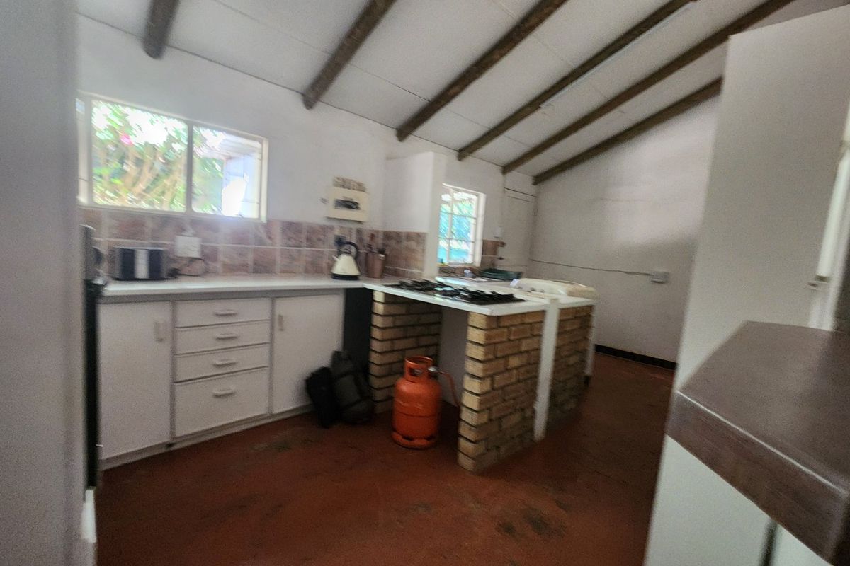 A rustic kitchen featuring exposed timber ceiling beams, a brick-based island with a gas hob, and tiled backsplash, offering potential for modernization.