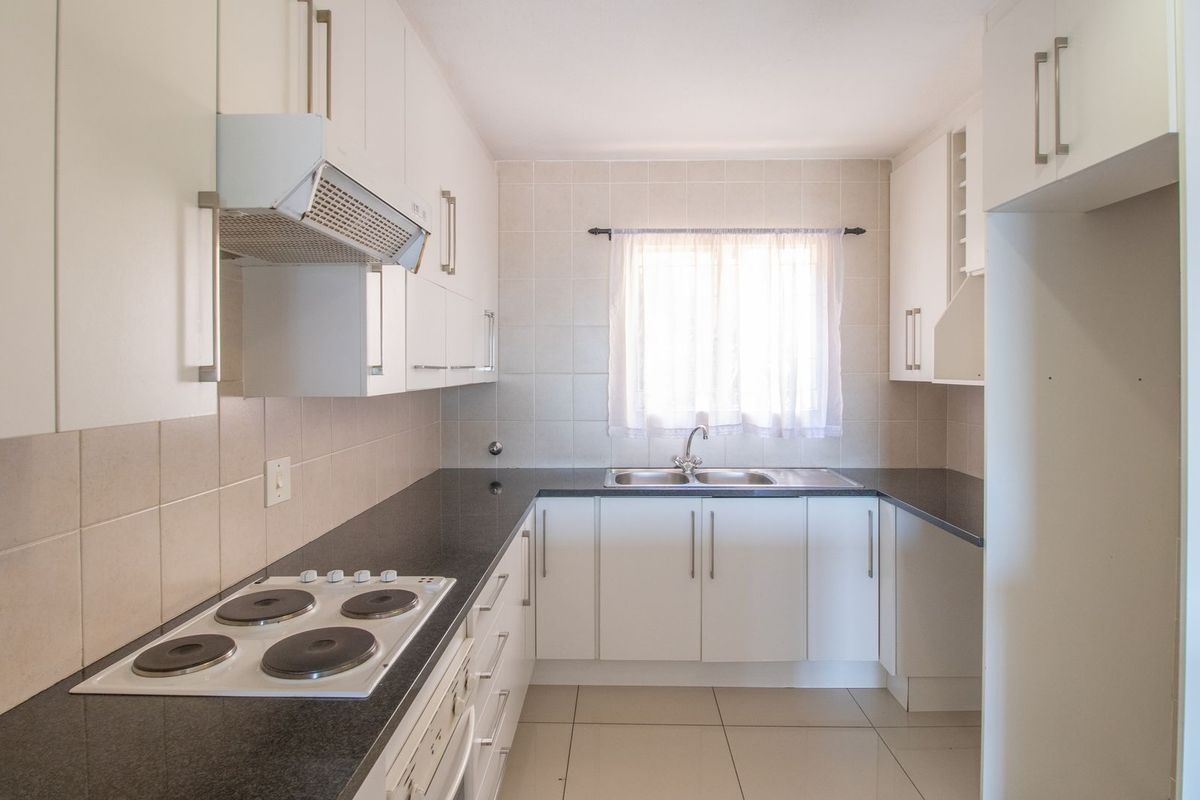 A clean, functional kitchen featuring white cabinetry, dark granite countertops, an electric hob with extractor fan, and tiled finishes throughout.