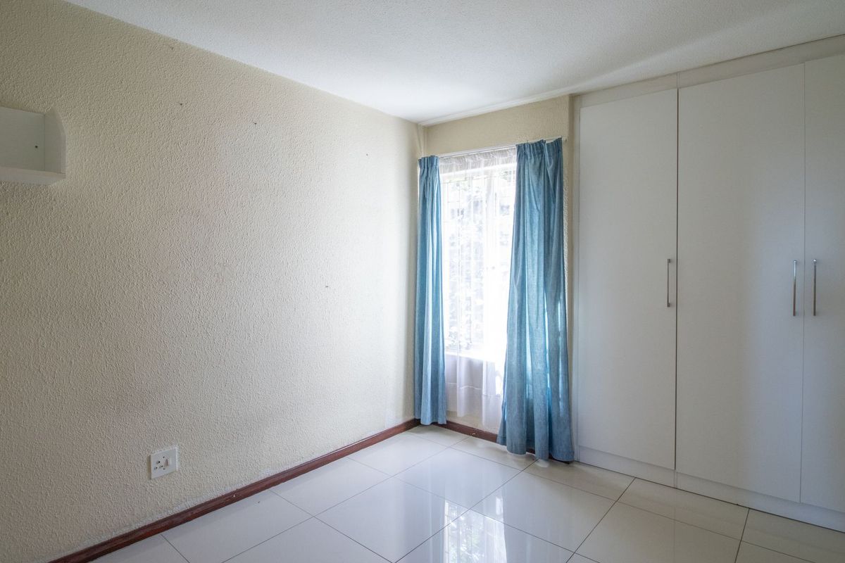 A bright, empty bedroom featuring tiled flooring, a built-in wardrobe, and a window with natural light.