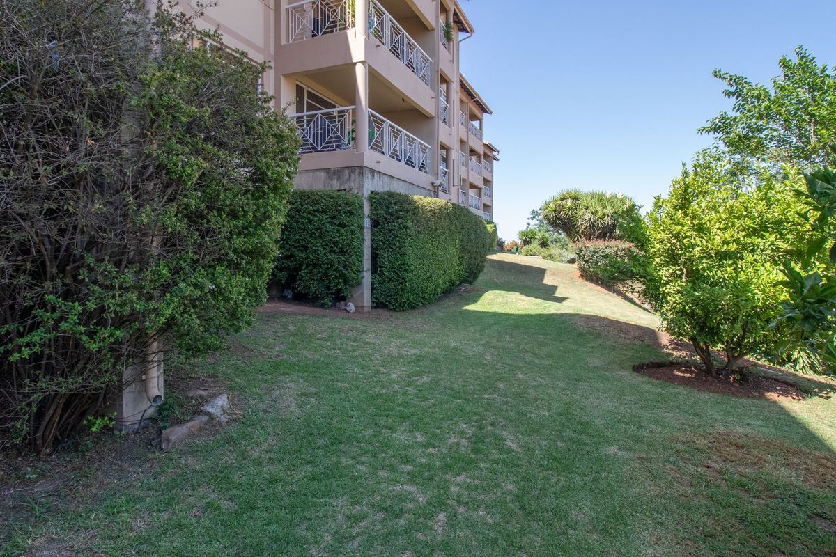 A view of the apartment building's rear elevation featuring balconies with metal railings overlooking a well-maintained lawn and landscaped garden area.