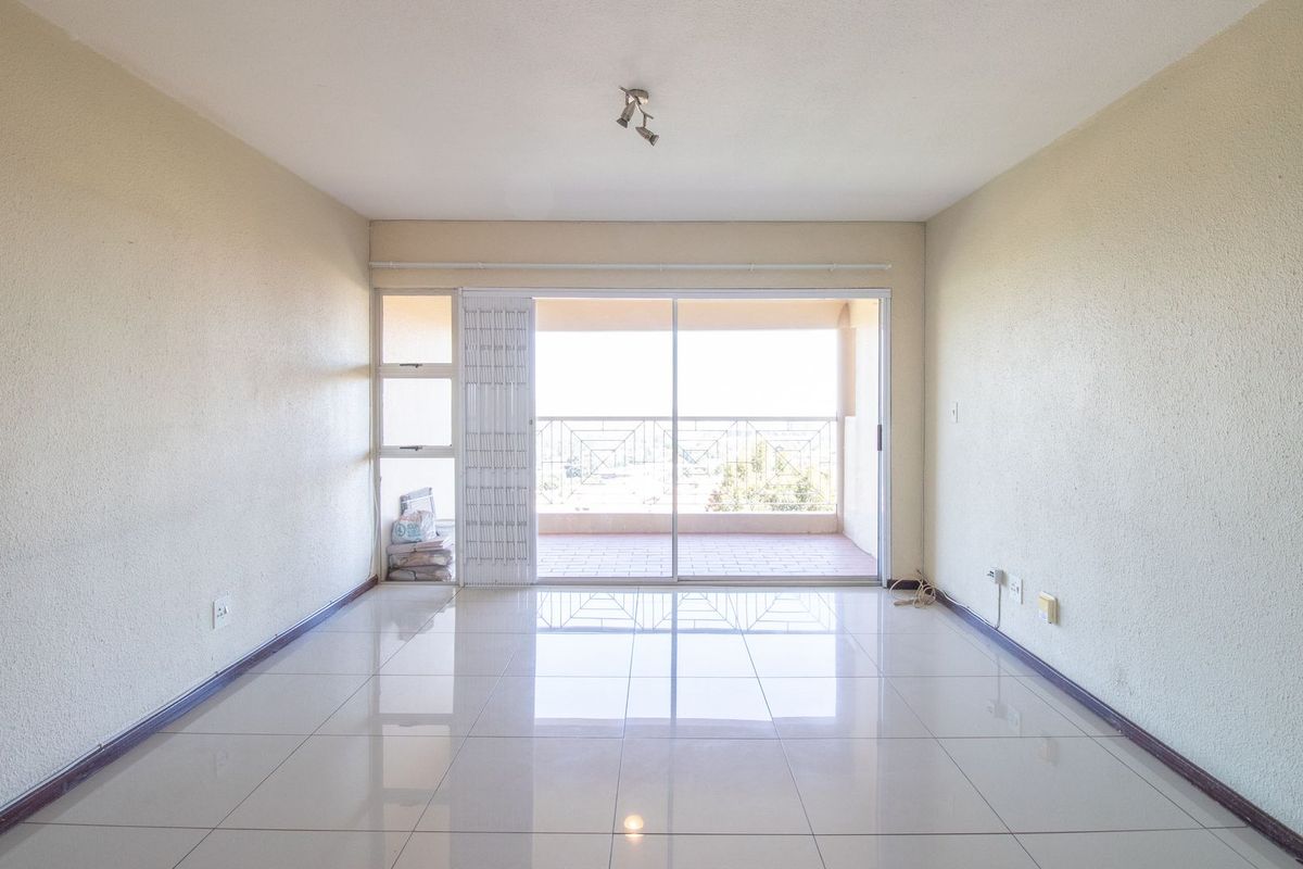 A bright, empty living room featuring polished tile flooring and a large sliding glass door that opens onto a private balcony.