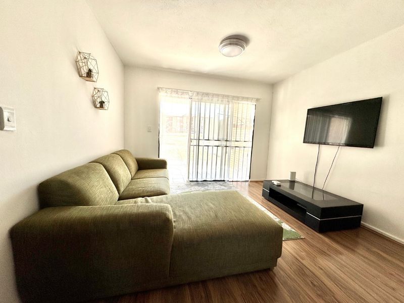 A bright living room featuring laminate flooring and a sliding glass door with a security gate, providing access to the outdoor area.