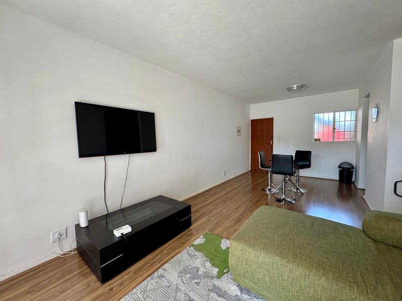 Open plan living and dining area featuring laminate flooring and a window with security bars.