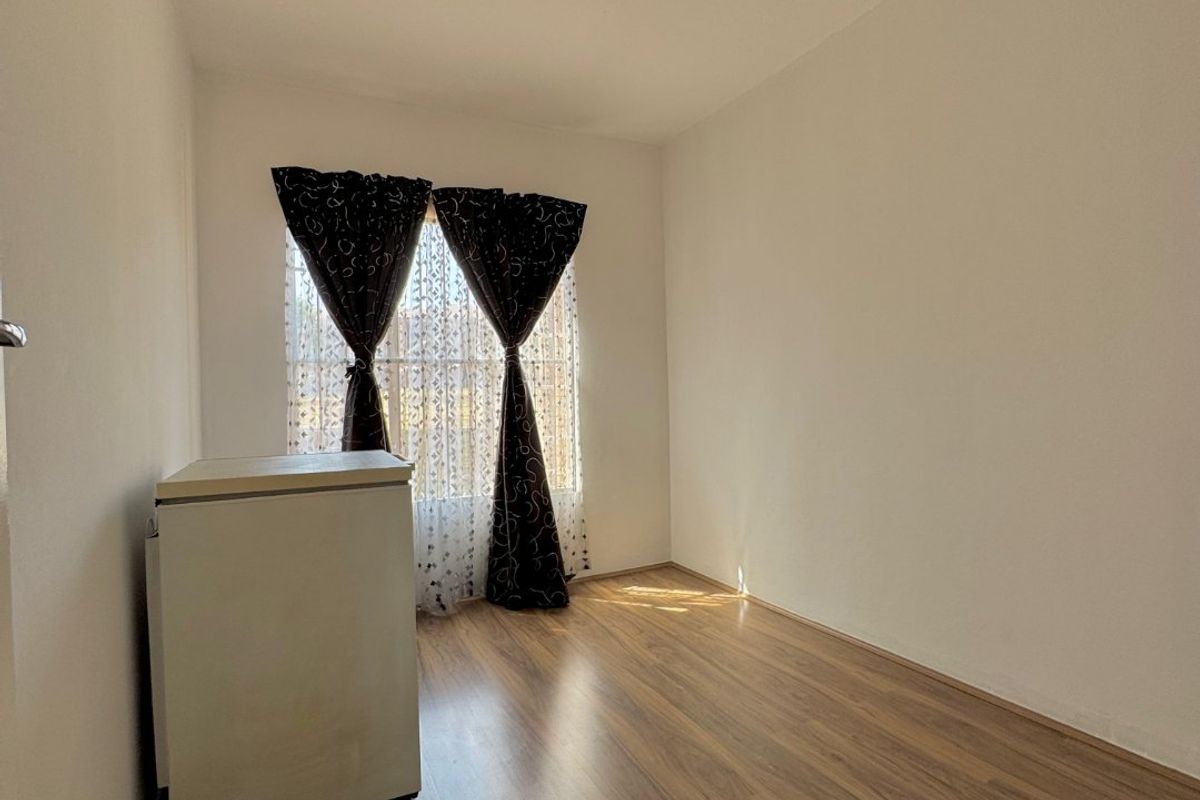 A bright, empty bedroom featuring wood-look laminate flooring and a simple ceiling light fixture, offering a clean canvas for personalization.