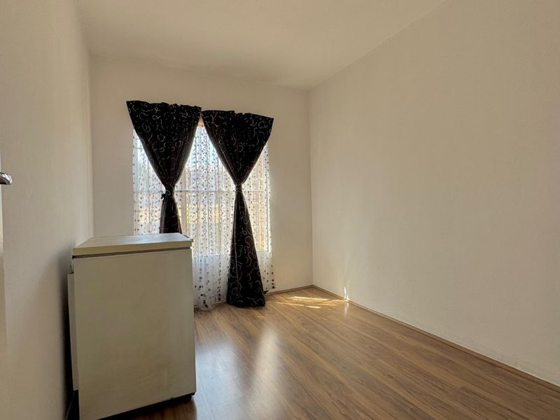A bright, empty bedroom featuring wood-look laminate flooring and a simple ceiling light fixture, offering a clean canvas for personalization.