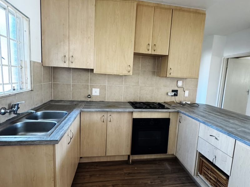 A functional kitchen featuring light wood-look cabinetry, laminate countertops, a built-in oven with gas hob, and a double bowl stainless steel sink.