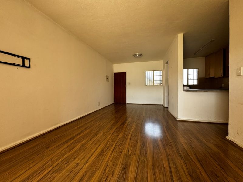 An empty open-plan living and kitchen area featuring laminate wood flooring, neutral walls, and a functional kitchen layout with built-in cabinetry.
