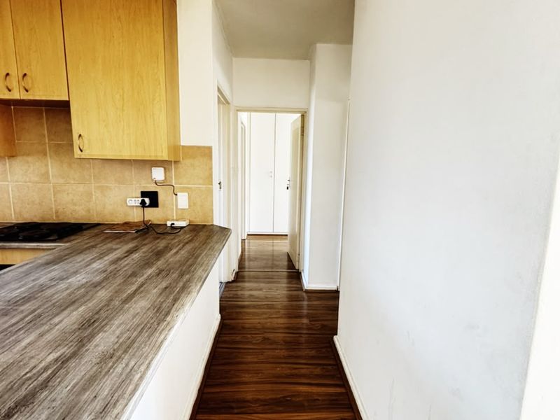 A functional kitchen area featuring laminate countertops, built-in cabinetry, and tiled backsplash, leading into a hallway with wood-look flooring.