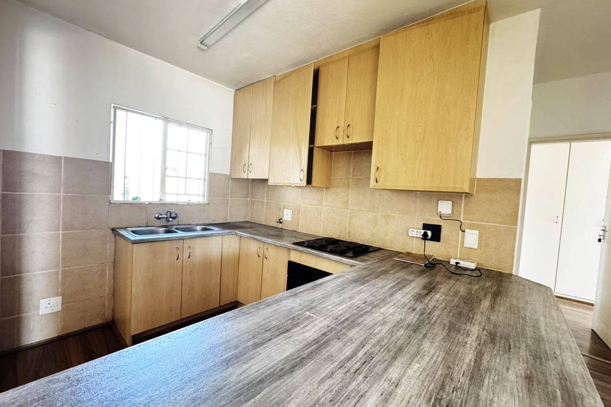 A functional kitchen featuring light wood cabinetry, a double basin sink, built-in hob, and a spacious laminate breakfast bar area.