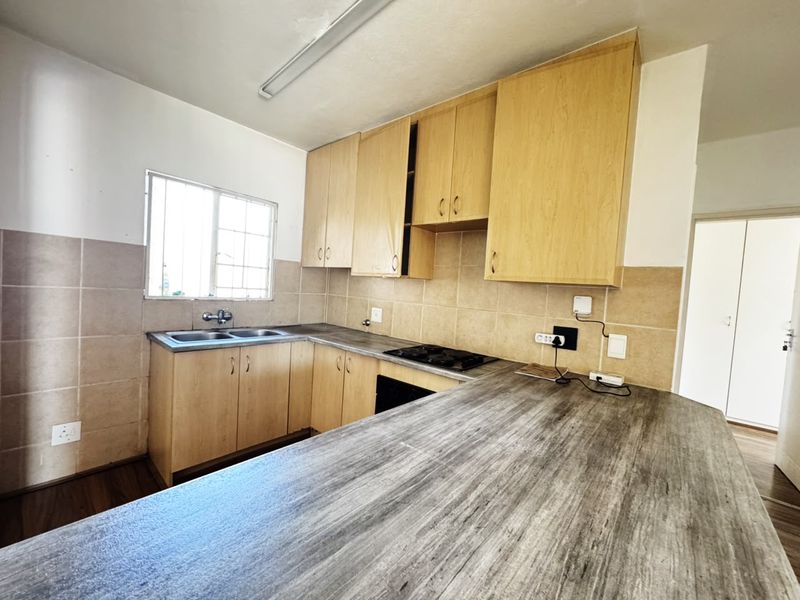 A functional kitchen featuring light wood cabinetry, a double basin sink, built-in hob, and a spacious laminate breakfast bar area.