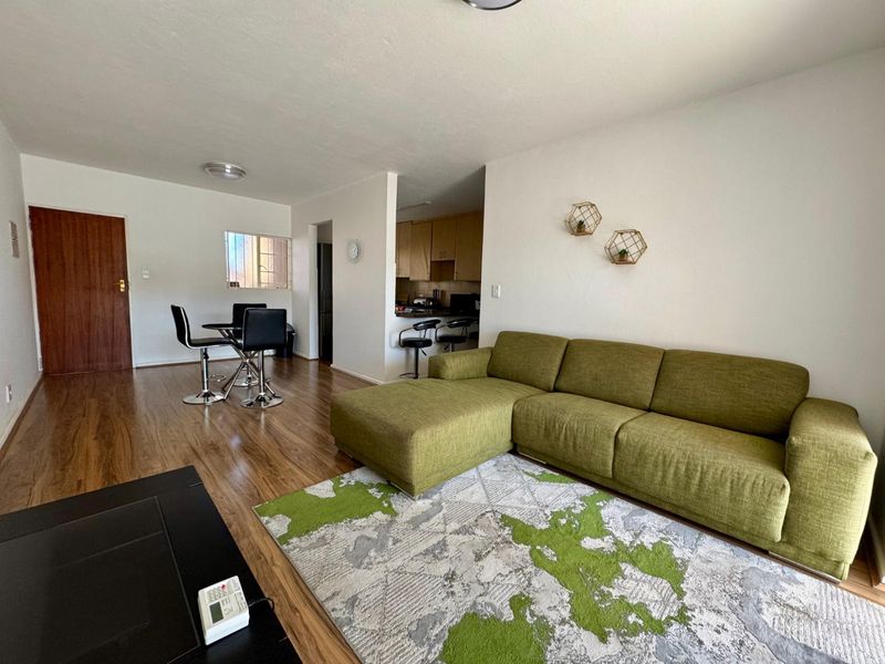 Open-plan living and dining area featuring laminate flooring and a functional kitchen with built-in cabinetry and a breakfast bar.