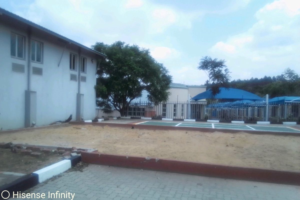 Rear exterior view of the commercial property featuring a paved driveway, perimeter fencing, and a partially developed sandy ground area with shade structures.