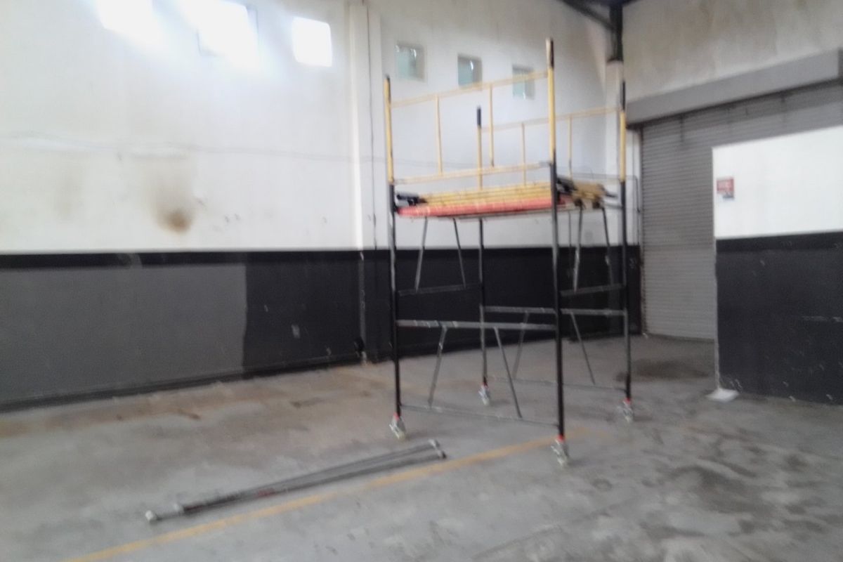 Spacious commercial utility or warehouse area featuring high ceilings, roller shutter access, and clerestory windows, currently in need of cosmetic refurbishment.