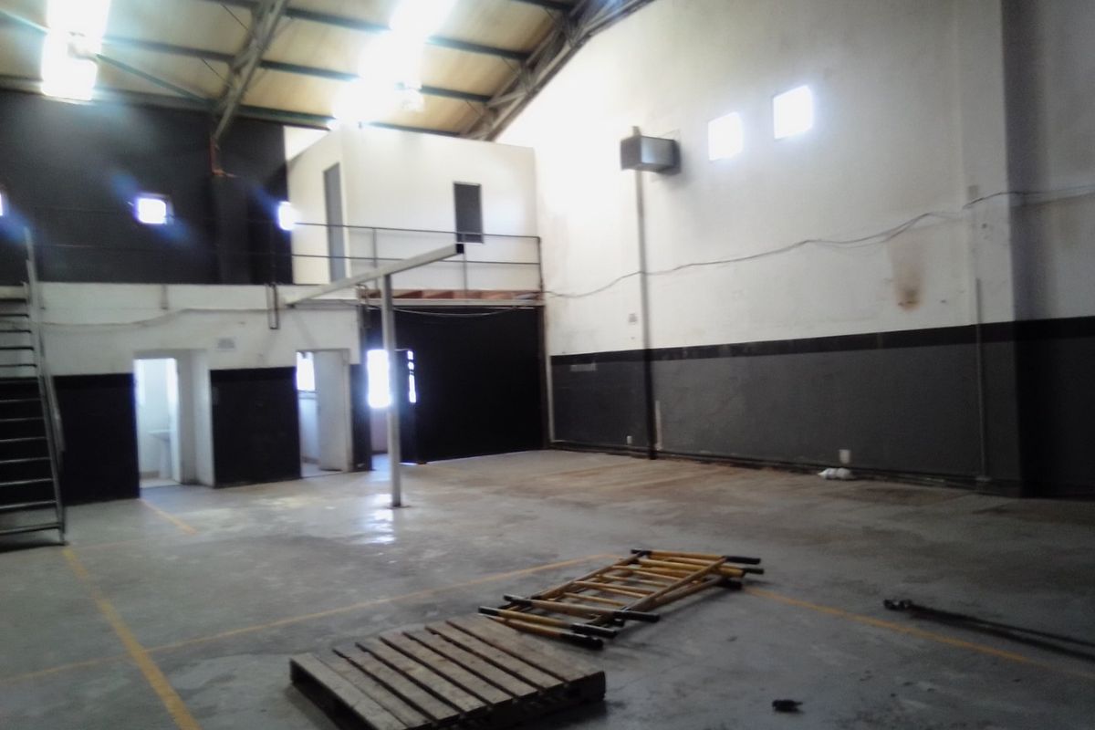 Spacious industrial utility area featuring high ceilings with exposed trusses, concrete flooring, and a mezzanine level, suitable for warehouse or workshop use.