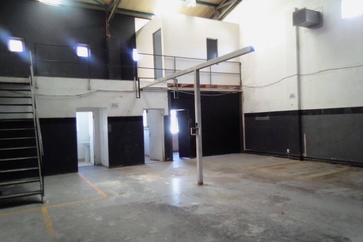 Spacious industrial utility area featuring a mezzanine level, metal staircase, and high ceilings with exposed trusses, suitable for warehouse or workshop use.