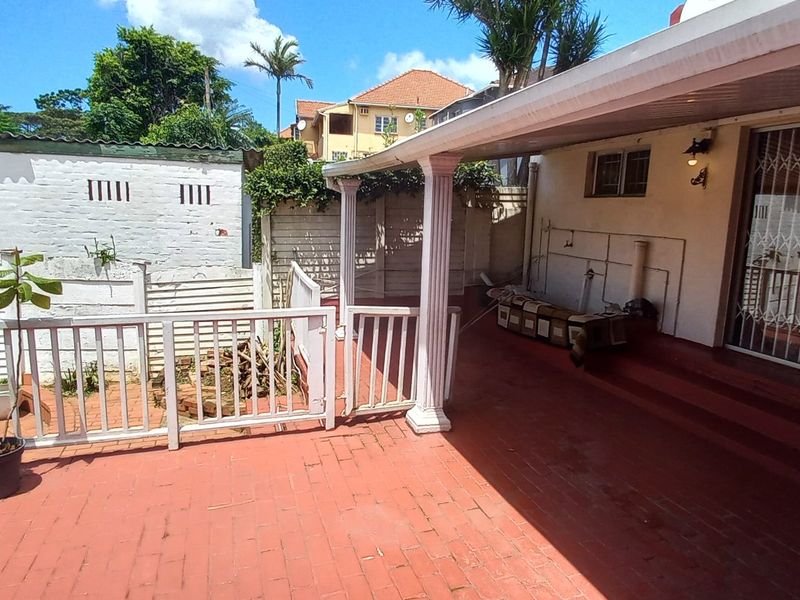 A covered outdoor patio area featuring brick paving, structural columns, and a security gate, providing a functional space for outdoor living.