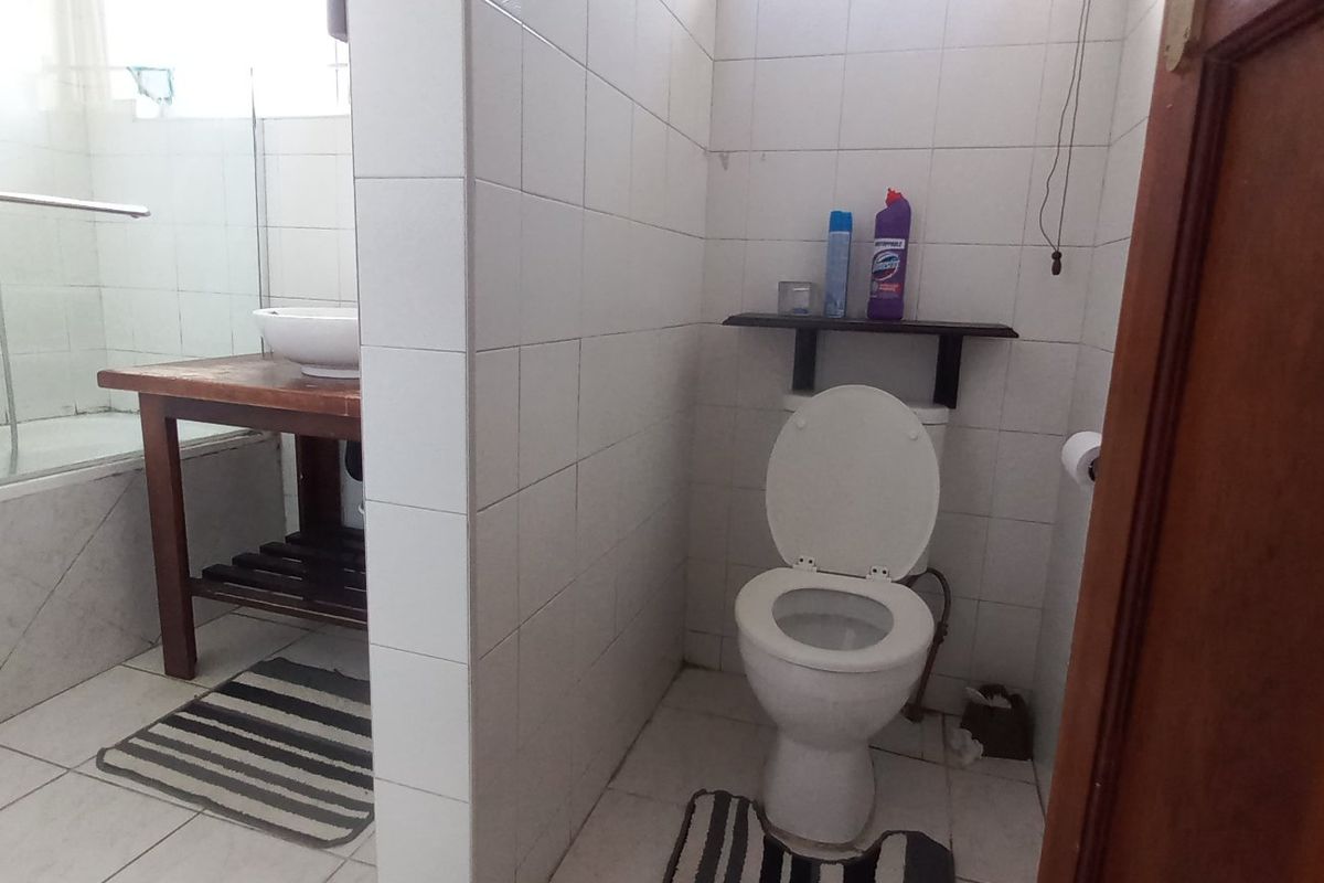 A functional bathroom featuring a bathtub with a glass screen, a separate toilet area, and tiled finishes throughout.