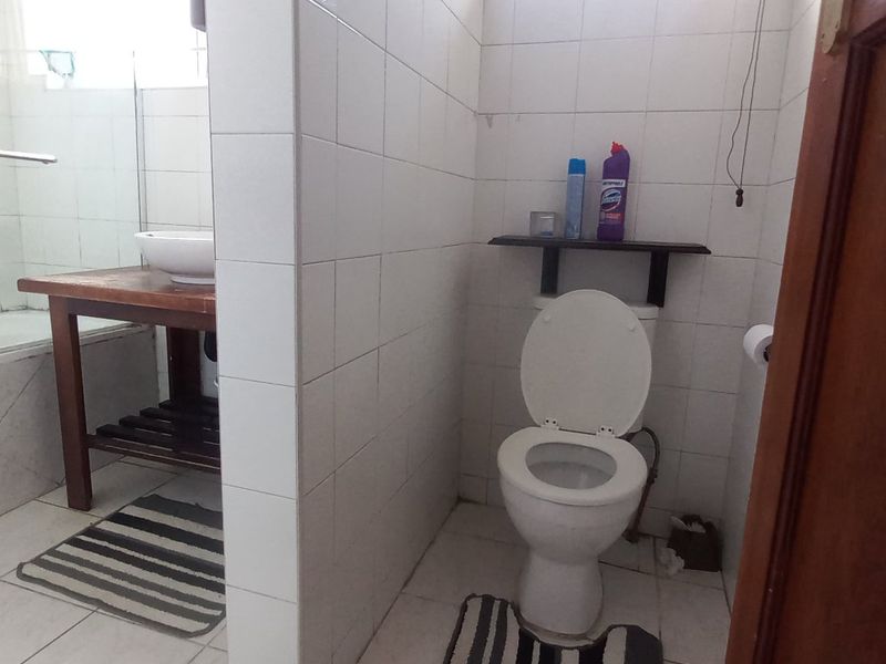 A functional bathroom featuring a bathtub with a glass screen, a separate toilet area, and tiled finishes throughout.