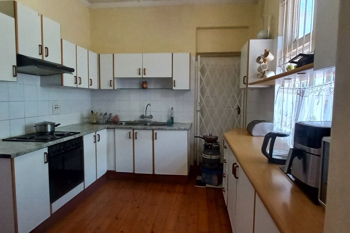 A functional kitchen featuring white built-in cabinetry, laminate countertops, a gas hob, and tiled splashbacks, offering a practical layout with potential for modern updates.