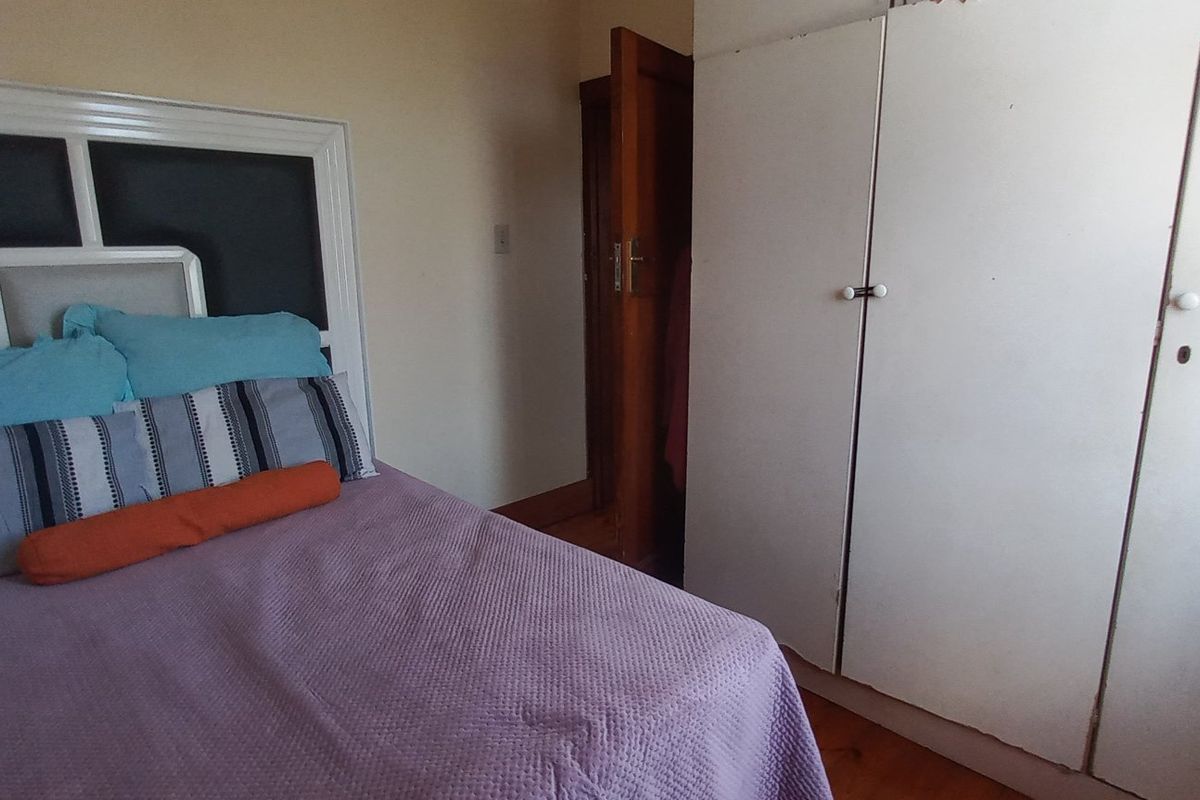 A bedroom featuring timber flooring and a built-in wardrobe with white cabinetry.