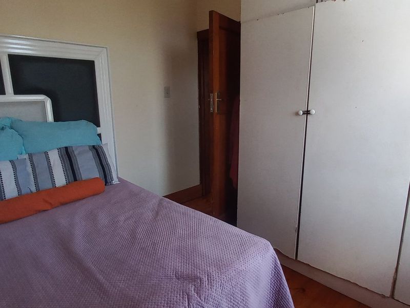 A bedroom featuring timber flooring and a built-in wardrobe with white cabinetry.