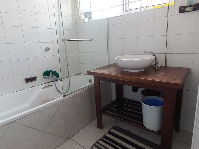A functional bathroom featuring a built-in bathtub with a glass screen and a vessel sink set on a wooden vanity unit.