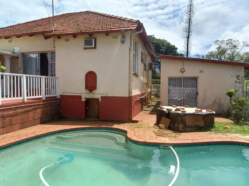 Rear exterior view featuring a swimming pool, raised patio area with white balustrades, and a detached garage structure.