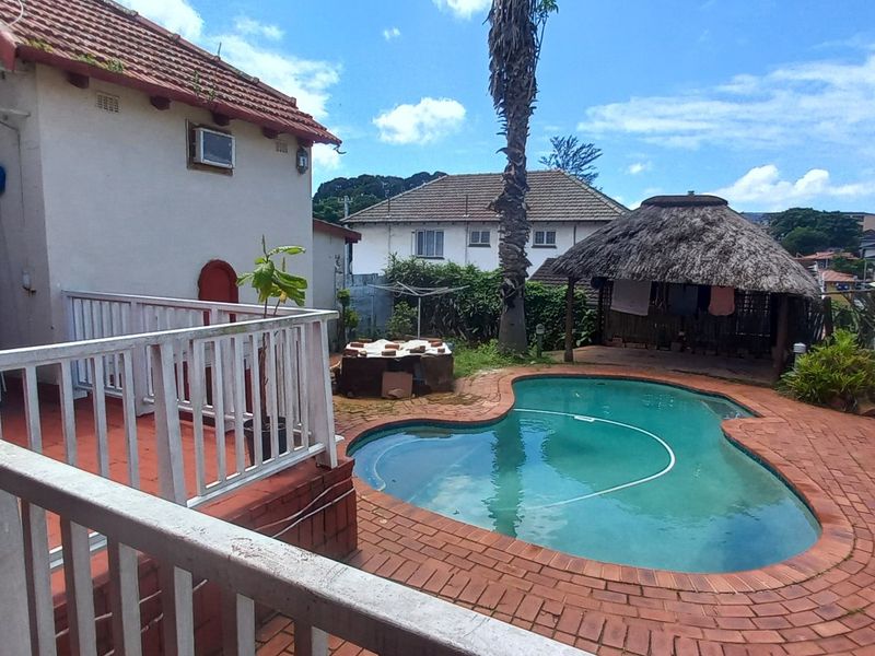 Rear outdoor area featuring a swimming pool, brick paved patio, and a traditional thatched lapa structure.