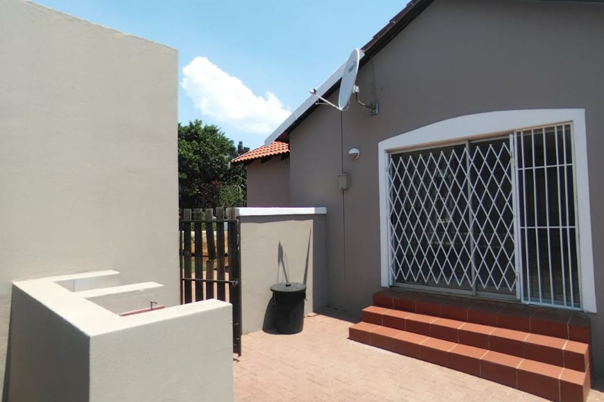 Rear exterior view featuring a paved patio area, brick steps leading to a sliding door with security gate, and a boundary wall.