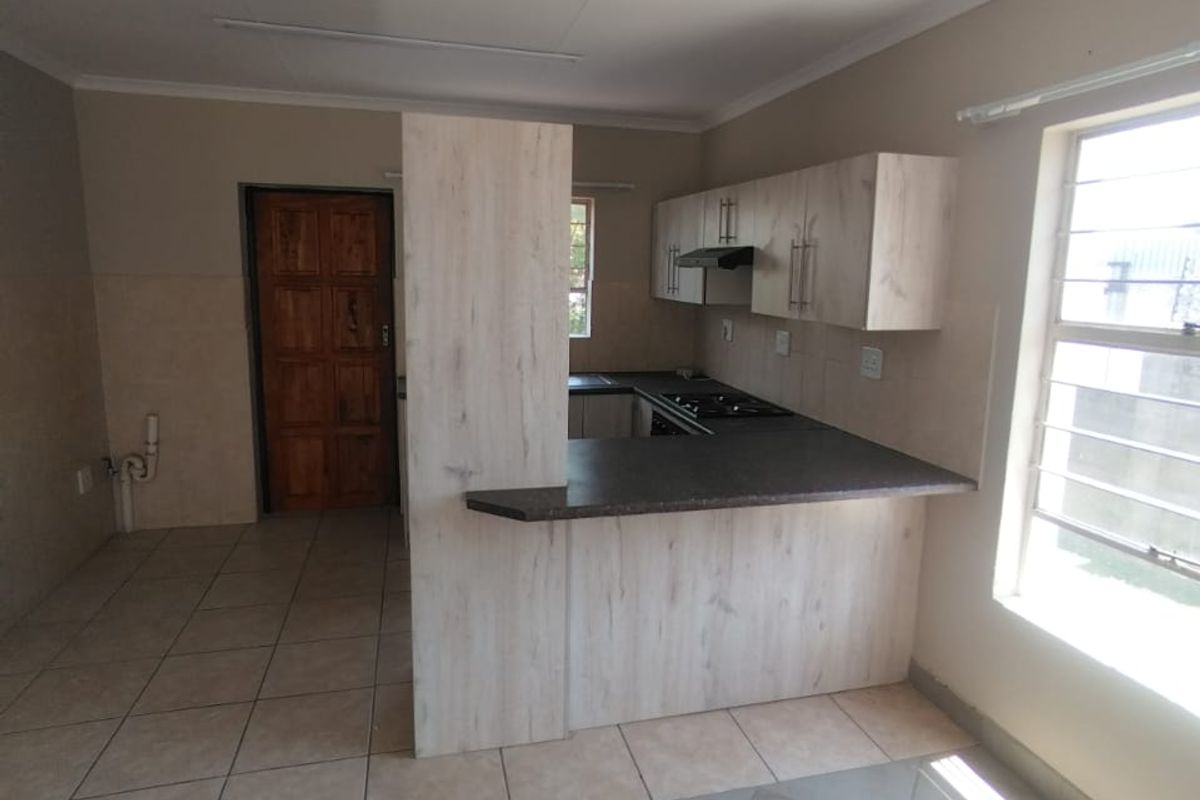 An empty kitchen featuring light wood-look cabinetry, dark countertops, a built-in gas hob with extractor, and tiled flooring throughout.